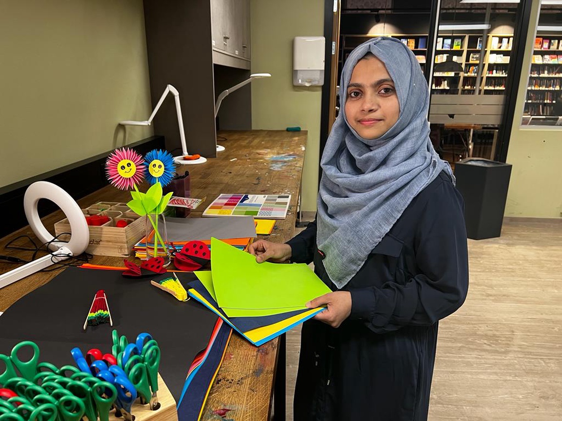 Bilde av Shamna som holder i papirer i forskjellige farger. I bakgrunnen ser vi papirblomster hun har brettet.