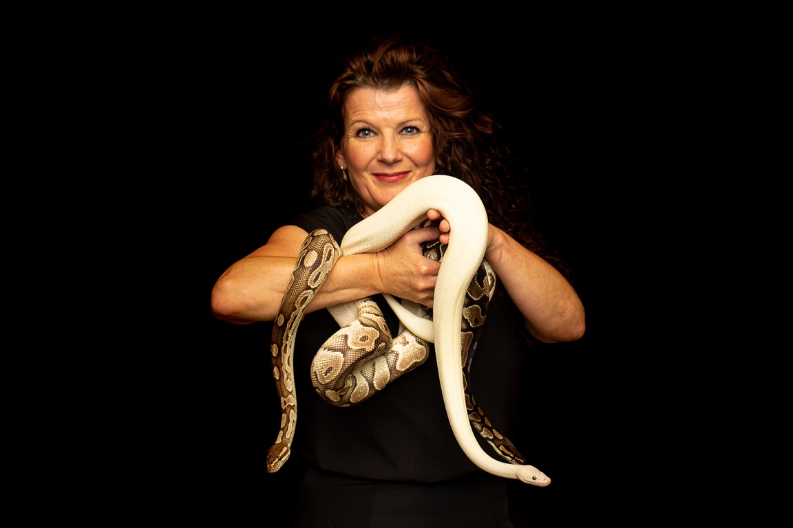 En kvinne holder en stor slange. Svart bakgrunn.