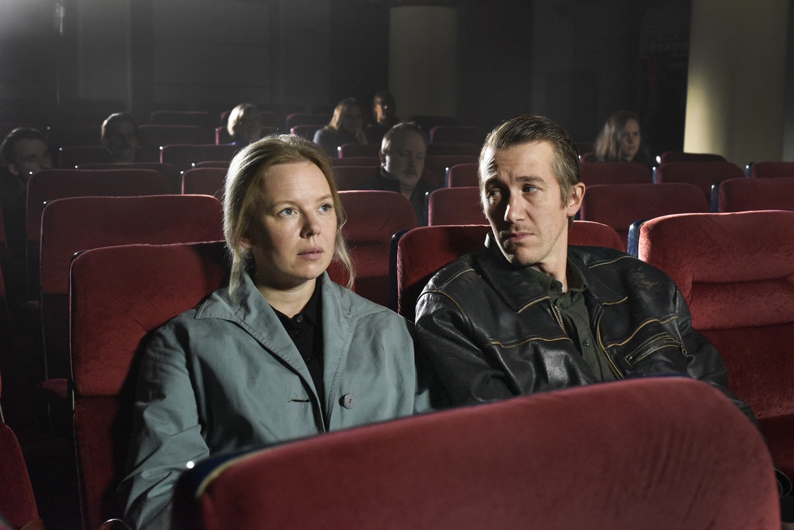 En kvinne og en mann sitter i en kinosal. Kvinnen ser på lerretet mens mannen ser på henne.