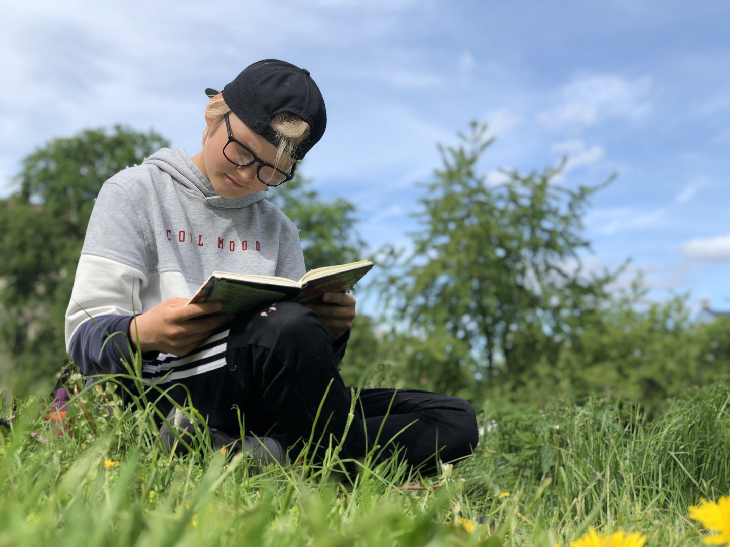 Gutt leser med bok på fanget i en grønn park